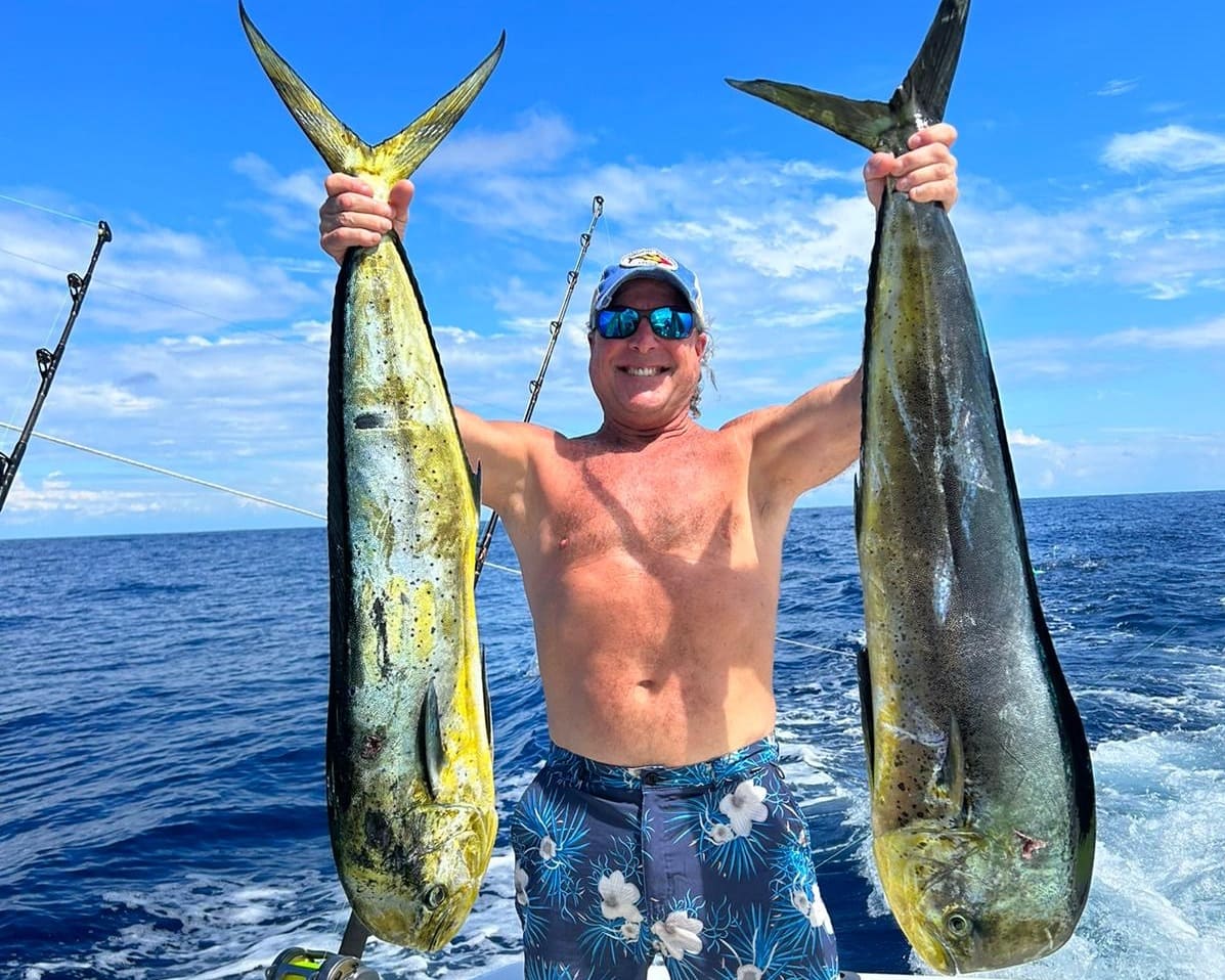 Man holding two fish on a fishing boat during a sportfishing tour in Jaco, Costa Rica